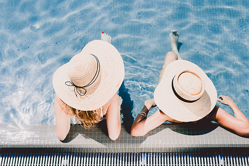 overhead view of two women in straw hats relaxing in swimming pool