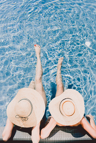 top view of two women in straw hats relaxing in swimming pool