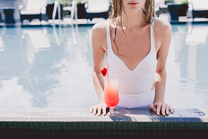 cropped view of wet woman in swimming pool with cool strawberry cocktail