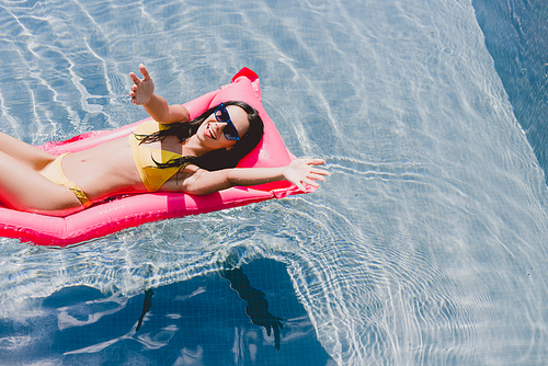happy brunette woman with outstretched hands on pool float in swimming pool