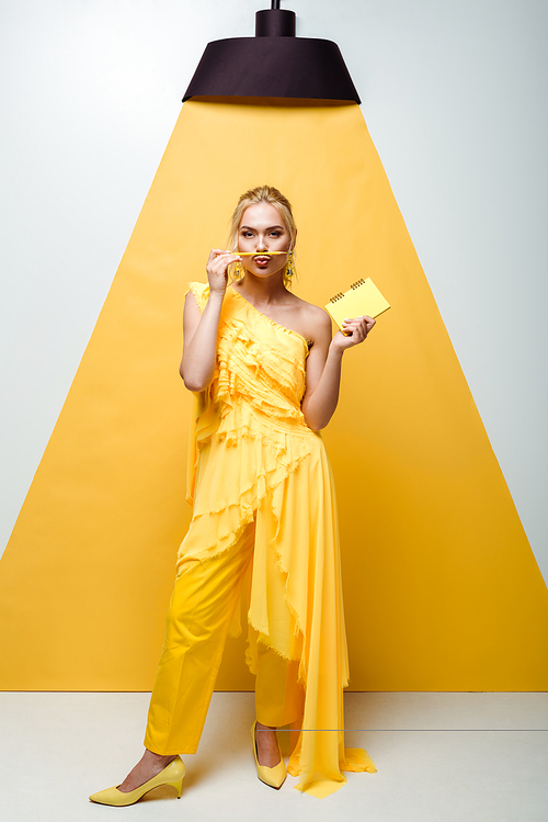 blonde woman with duck face holding pencil near mouth and notebook in hand on white and yellow