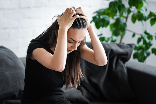 frustrated young woman suffering from depression while sitting on couch and holding hands on head