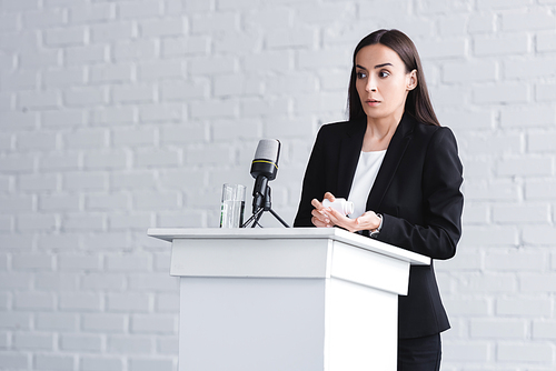 pretty lecturer, suffering from glossophobia, standing on podium tribune and holding container with pills