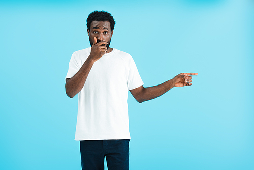 shocked african american man in white t-shirt pointing aside isolated on blue