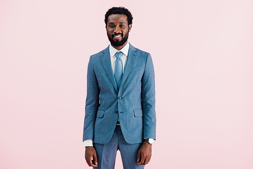 smiling african american businessman in suit, isolated on pink