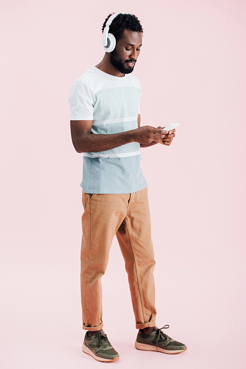 african american man listening music with headphones and smartphone, isolated on pink