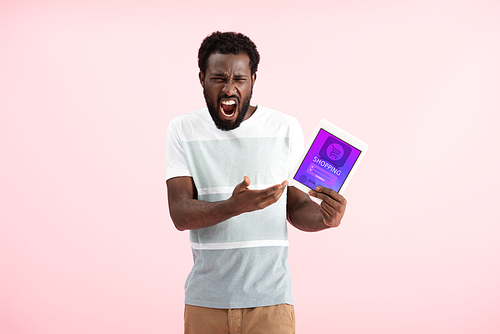 emotional african american man screaming and showing digital tablet with shopping app, isolated on pink