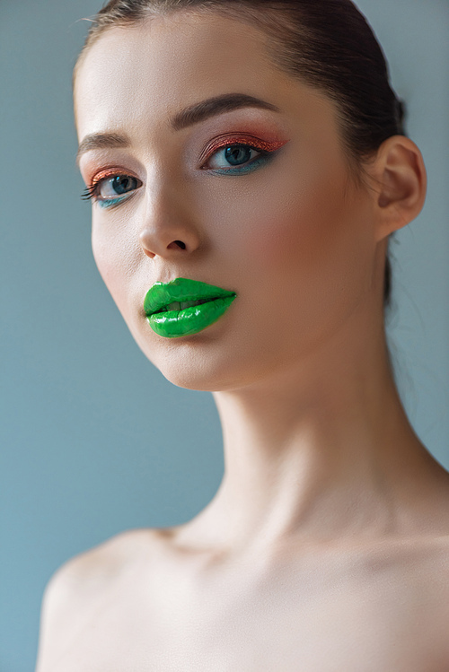 portrait of beautiful naked woman with green lips, pink and blue eyeshadow isolated on blue