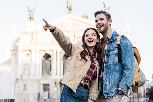 Man with hand in pocket smiling with excited woman pointing with finger in city