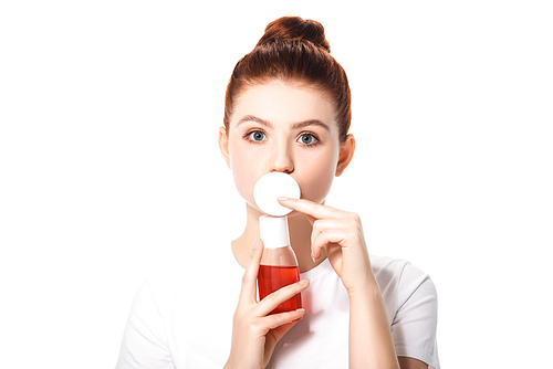 surprised teenager with clean skin holding cotton sponge and bottle with red makeup remover, isolated on white