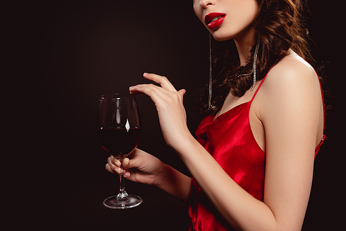 Cropped view of elegant young woman holding glass of red wine isolated on black