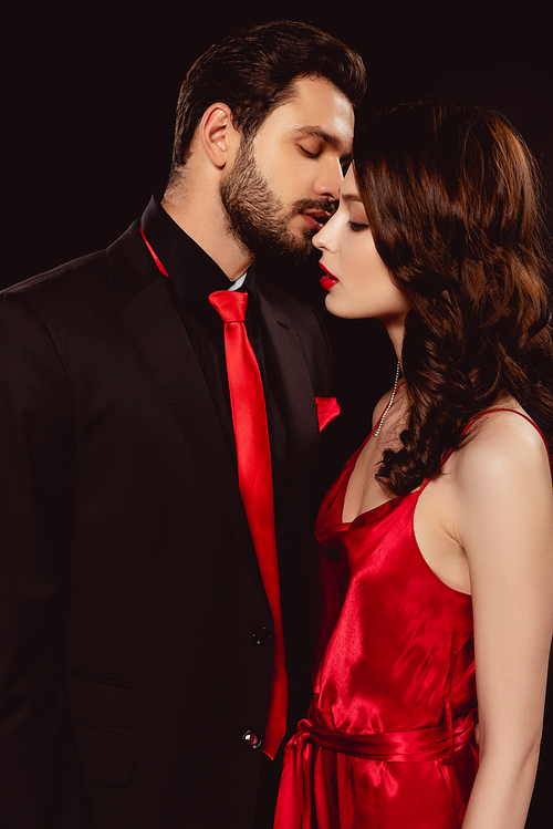 Side view of handsome man kissing beautiful girlfriend in dress isolated on black