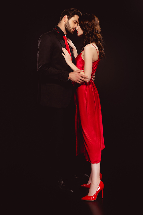 Side view of handsome man embracing beautiful girlfriend in red dress isolated on black