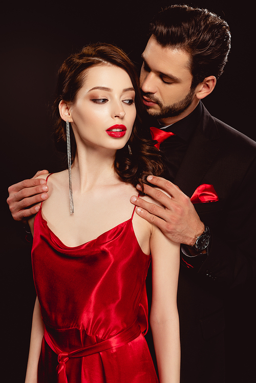 Elegant man in formal wear hugging beautiful girlfriend in red dress isolated on black