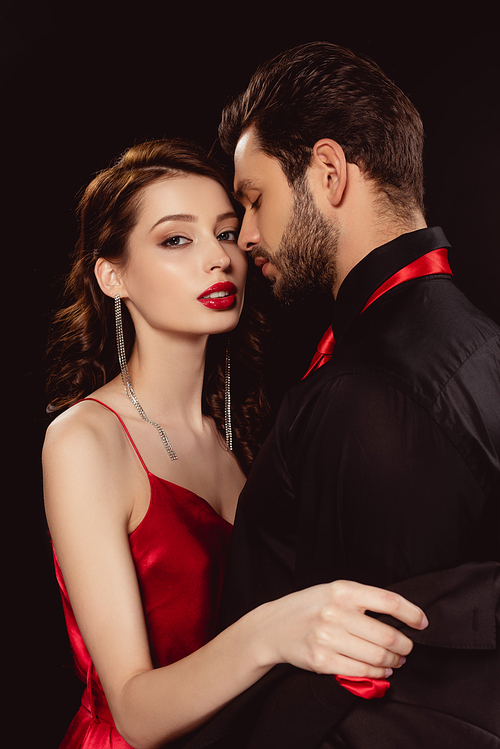 Side view of elegant girl with red lips taking off jacket of boyfriend and  isolated on black