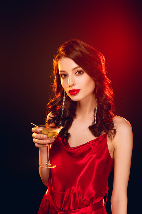 Beautiful woman in red dress holding glass of cocktail on black background with lighting