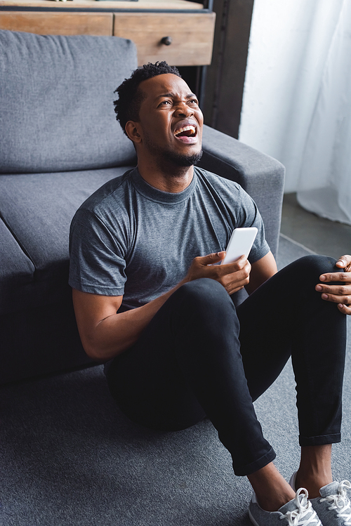 stressed african american man screaming and using smartphone at home