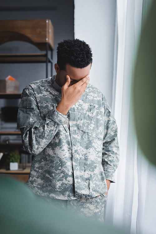 selective focus of lonely sad african american soldier in military uniform at home