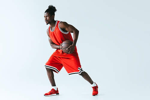 african american basketball player in red sportswear holding ball on grey background