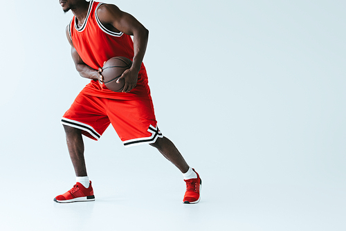 partial view of african american sportsman in red sportswear playing basketball on grey background