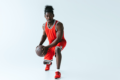 handsome african american sportsman in red sportswear playing basketball on grey background