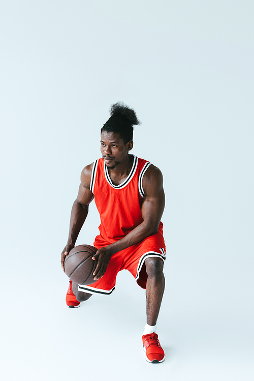african american basketball player in red sportswear holding ball on grey background