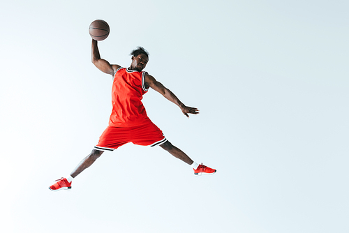 african american sportsman jumping while playing basketball isolated on grey