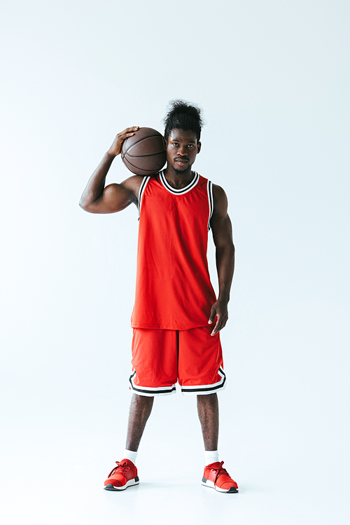 confident african american basketball player in red sportswear holding ball and  on grey background