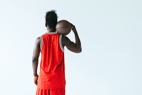 back view of african american basketball player in red sportswear holding ball isolated on grey