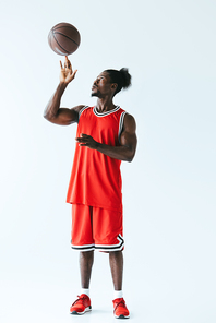 handsome african american basketball player playing with ball on grey background