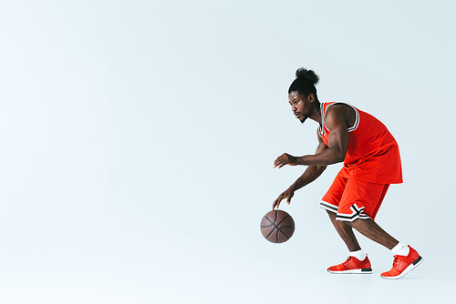 handsome african american sportsman playing basketball on grey background with copy space