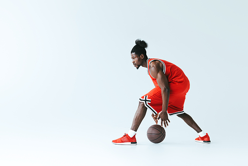 athletic african american sportsman playing basketball on grey background