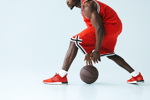 cropped view of african american sportsman in red sportswear playing basketball on grey background