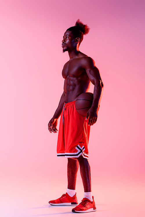 handsome african american basketball player looking away on pink and purple gradient background with lighting