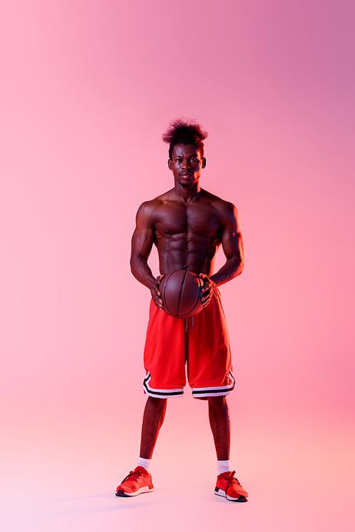confident african american basketball player with muscular torso  on pink and purple gradient background with lighting