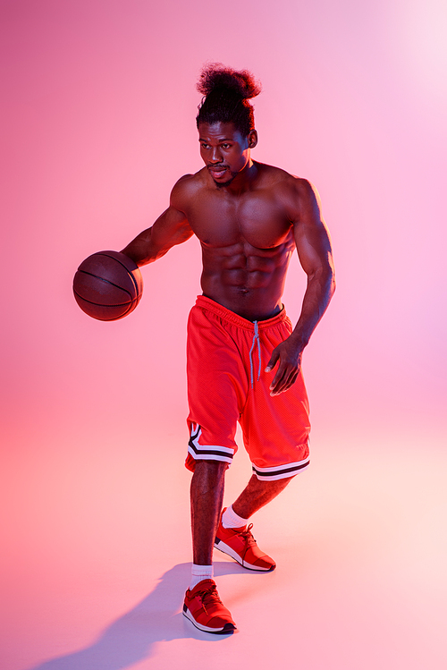shirtless african american sportsman in red shorts playing basketball on pink background with gradient and lighting
