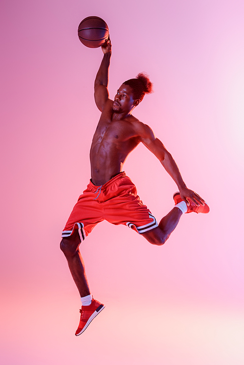 african american sportsman with muscular torso playing basketball on pink and purple gradient background