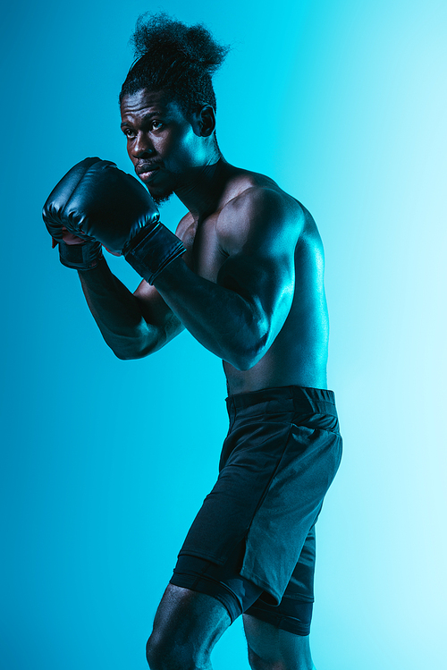 confident african american sportsman with muscular torso boxing on blue background