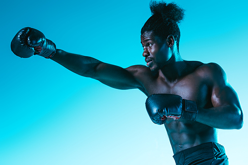 confident african sportsman in boxing gloves training on blue background