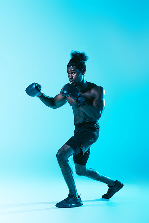 confident african american sportsman in shorts and sneakers boxing on blue background