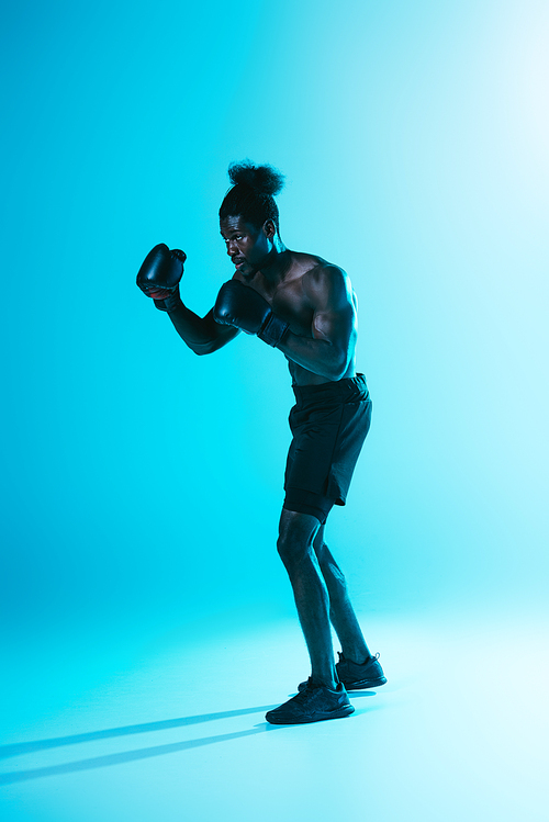 serious african american sportsman in shorts and sneakers boxing on blue background