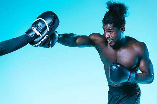 african american boxer working out with trainer on blue background
