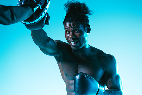 muscular african american boxer working out with trainer on blue background