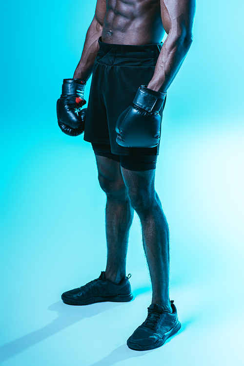 partial view of african american sportsman in shorts and boxing gloves on blue background