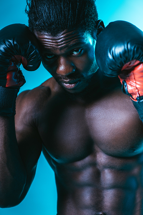 confident african american sportsman in boxing gloves  on blue background