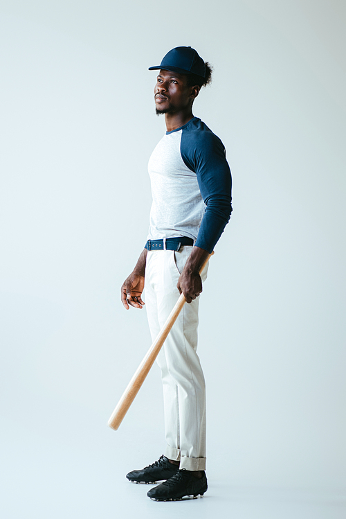 handsome african american sportsman looking away while holding baseball bat on grey background
