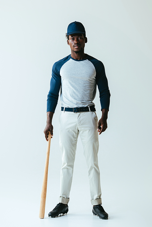 handsome african american baseball player posing at camera on grey background
