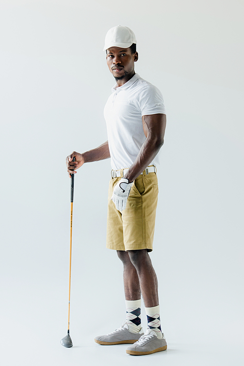 handsome african american sportsman holding golf club on grey background