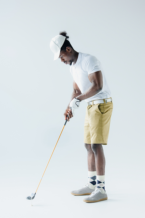 handsome african american sportsman playing golf on grey background