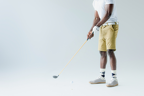 cropped view of african american sportsman in shorts playing golf on grey background